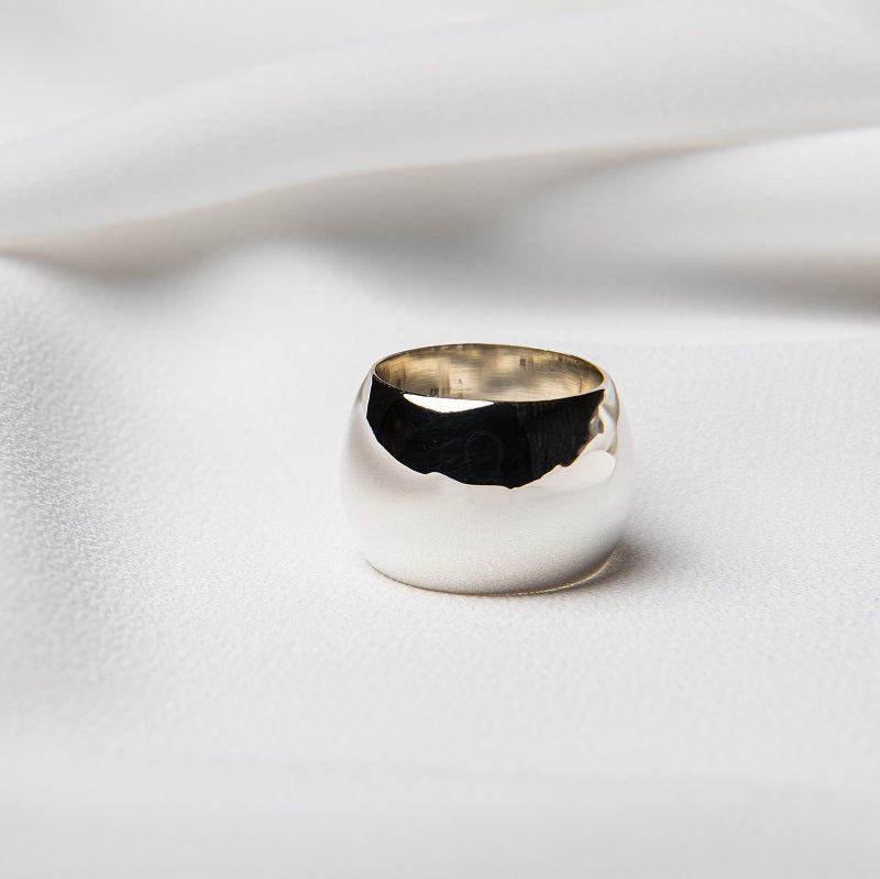 A polished silver band ring on a white textured surface.