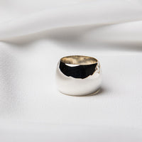 A polished silver band ring on a white textured surface.