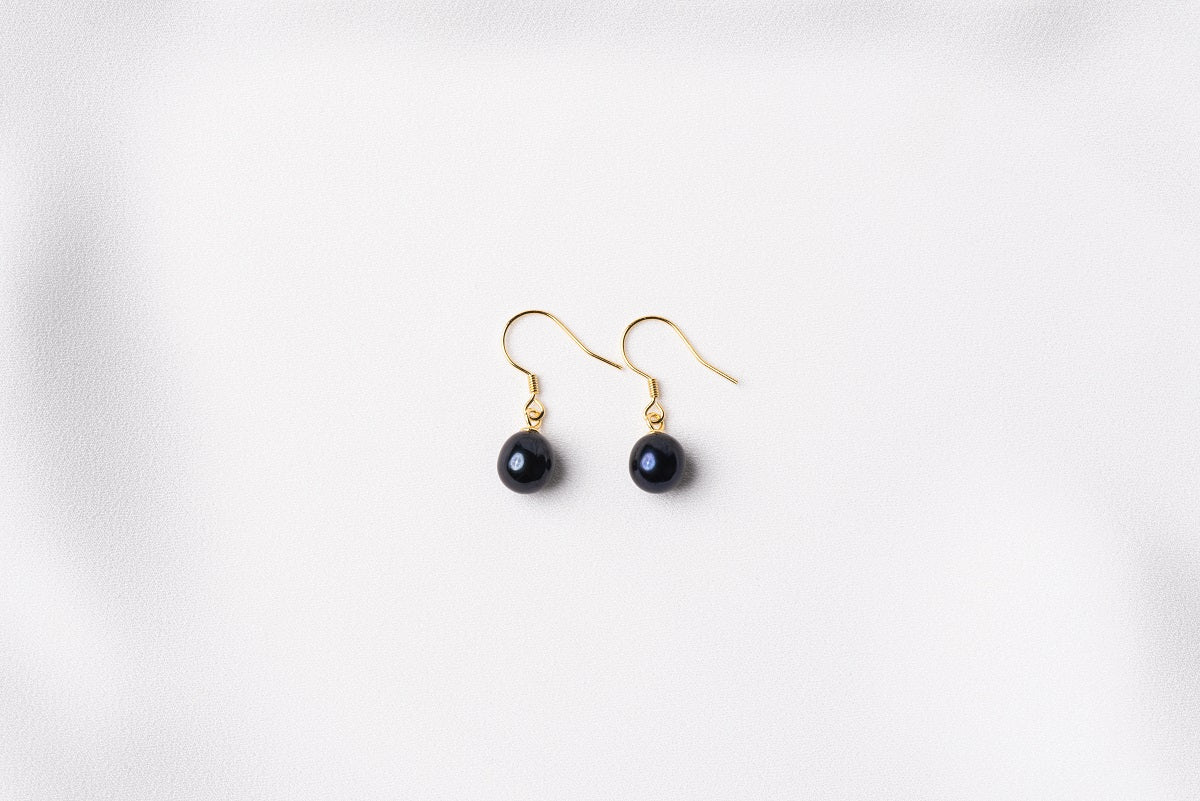 A pair of pearl earrings dangled from silver hooks, placed on a white background