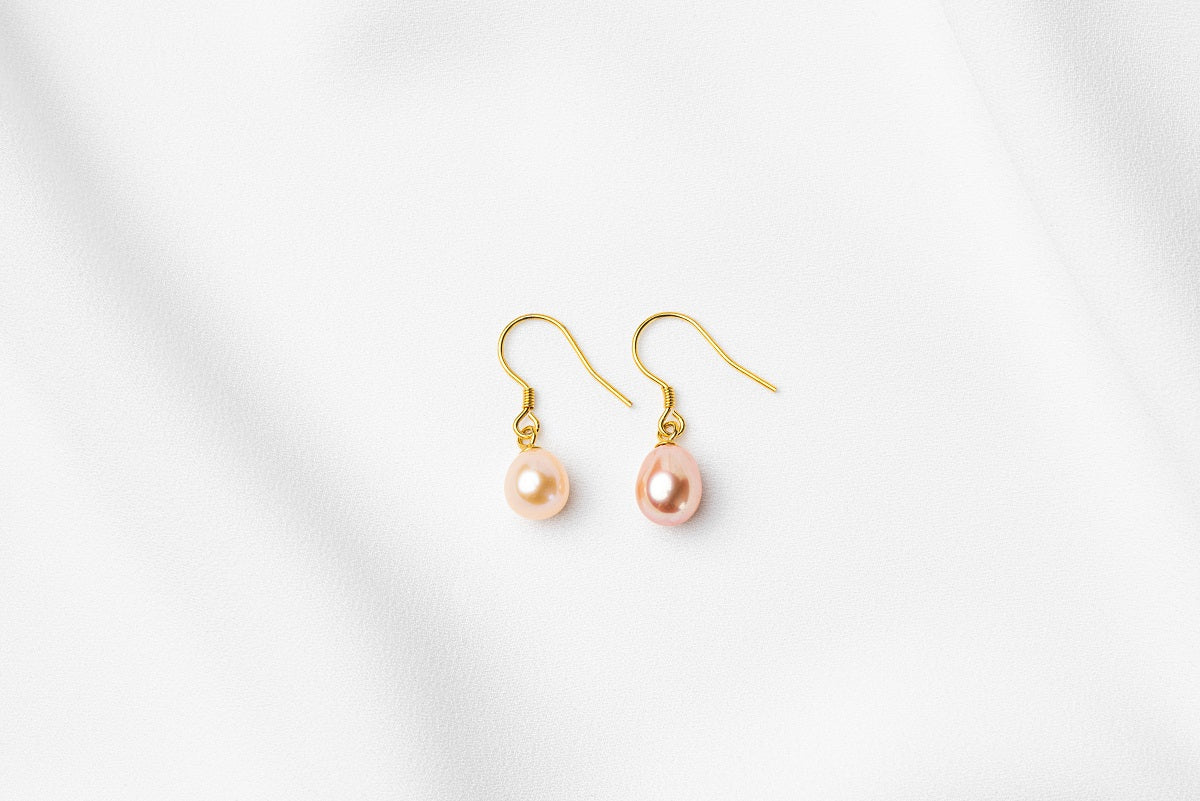 A pair of pearl earrings dangled from gold vermeil hooks, placed on a white background