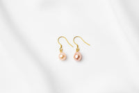 A pair of pearl earrings dangled from gold vermeil hooks, placed on a white background