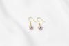 A pair of pearl earrings dangled from gold vermeil hooks, placed on a white background