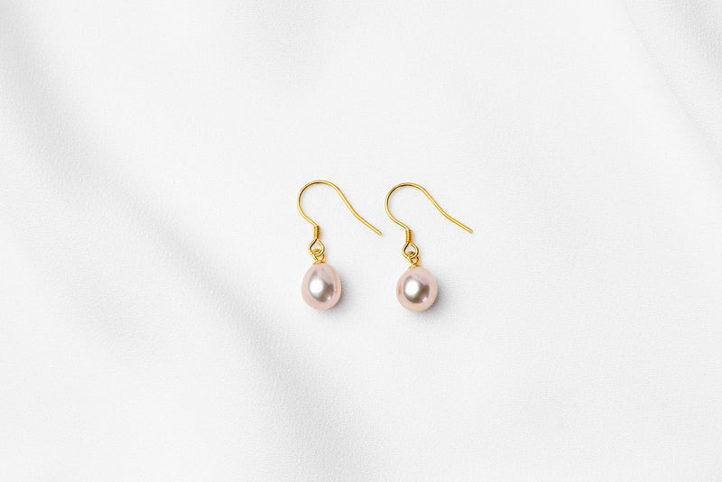 A pair of pearl earrings dangled from gold vermeil hooks, placed on a white background