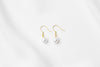A pair of pearl earrings dangled from gold vermeil hooks, placed on a white background