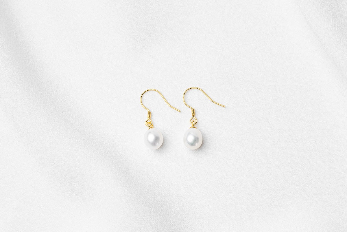 A pair of pearl earrings dangled from gold vermeil hooks, placed on a white background