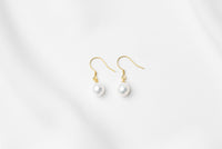 A pair of pearl earrings dangled from gold vermeil hooks, placed on a white background