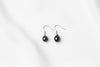 A pair of pearl earrings dangled from silver hooks, placed on a white background