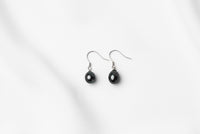 A pair of pearl earrings dangled from silver hooks, placed on a white background