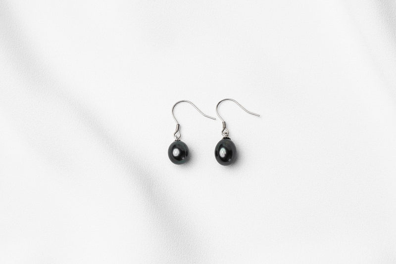 A pair of pearl earrings dangled from silver hooks, placed on a white background