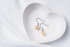 A pair of champagne pearl earrings dangled from silver hooks, placed inside a white, heart-shaped dish.