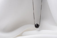 An image of a classic black pearl necklace with an adjustable chain and a single pearl pendant, displayed on a white fabric surface.