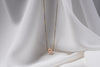 An image of a classic champagne pearl necklace with an adjustable chain and a single pearl pendant, displayed on a white fabric surface.