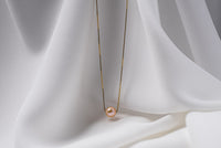 An image of a classic champagne pearl necklace with an adjustable chain and a single pearl pendant, displayed on a white fabric surface.