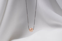 An image of a classic champagne pearl necklace with an adjustable chain and a single pearl pendant, displayed on a white fabric surface.