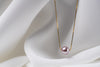 An image of a classic lavender pearl necklace with an adjustable chain and a single pearl pendant, displayed on a white fabric surface.