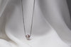 An image of a classic lavender pearl necklace with an adjustable chain and a single pearl pendant, displayed on a white fabric surface.
