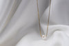 An image of a classic pearl necklace with an adjustable chain and a single pearl pendant, displayed on a white fabric surface.