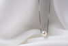 An image of a classic white pearl necklace with an adjustable chain and a single pearl pendant, displayed on a white fabric surface.
