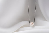 An image of a classic white pearl necklace with an adjustable chain and a single pearl pendant, displayed on a white fabric surface.