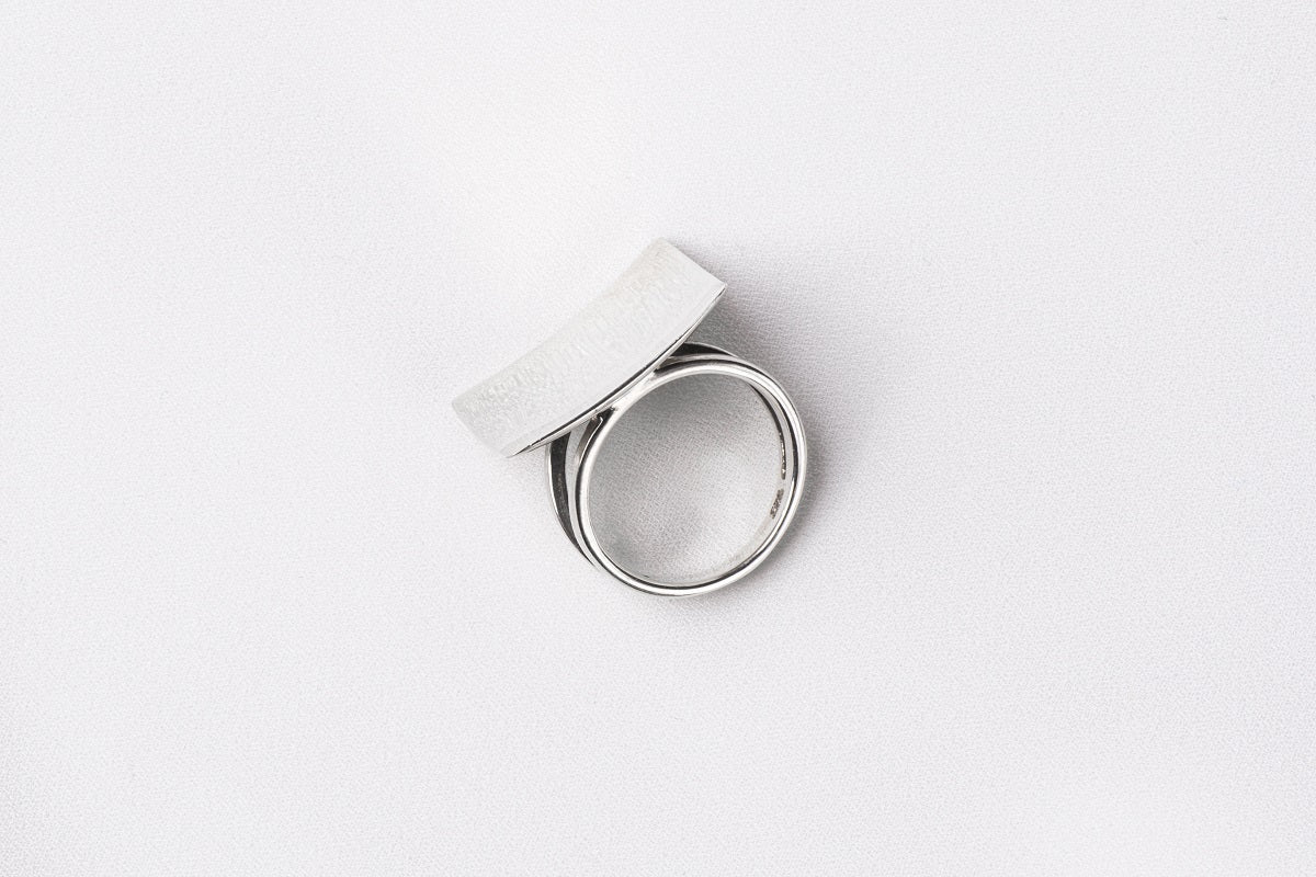 A polished silver ring with a concave design, displayed on a white surface.