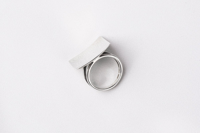 A polished silver ring with a concave design, displayed on a white surface.