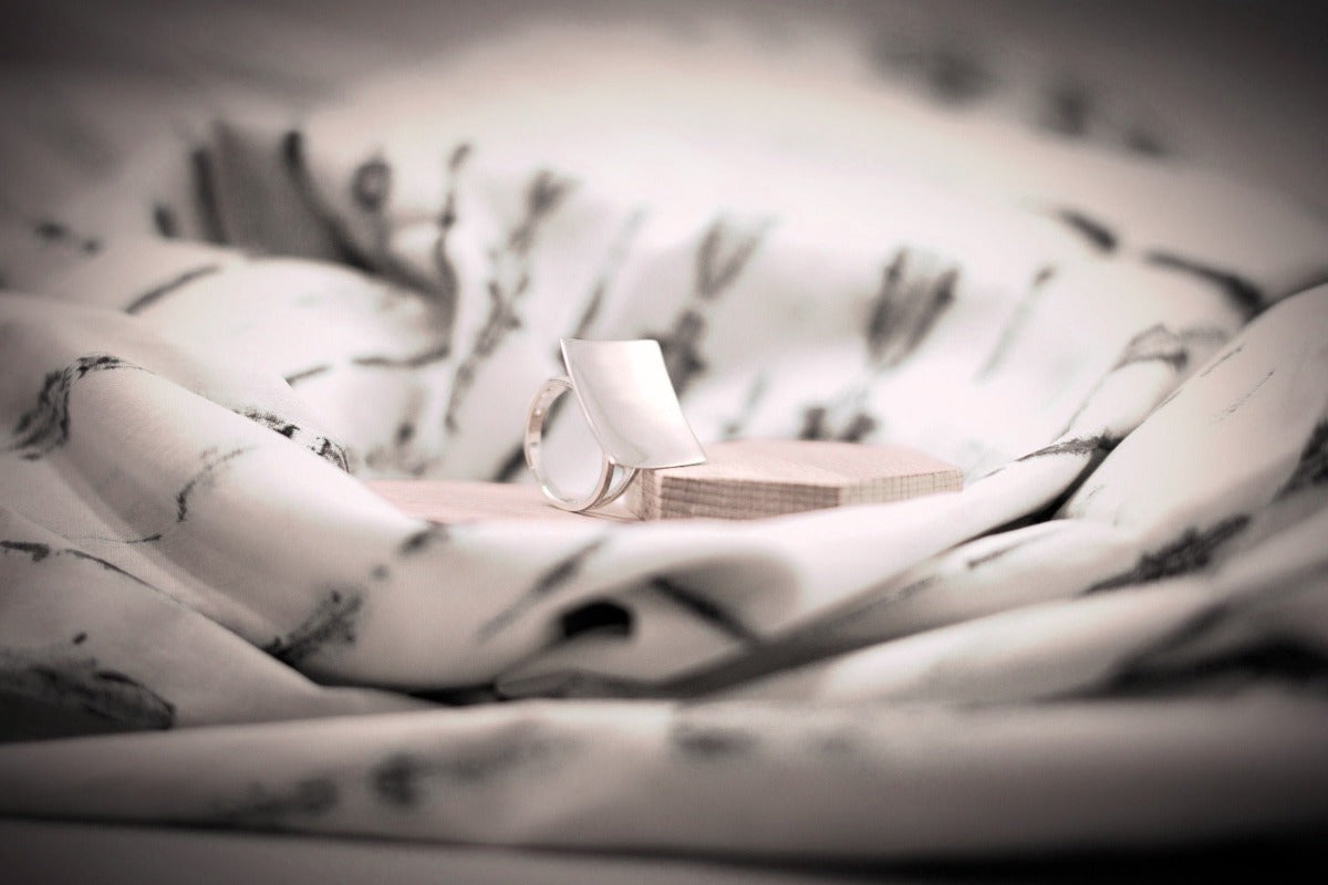 A polished silver ring with a concave design, displayed on a textured surface
