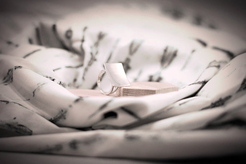 A polished silver ring with a concave design, displayed on a textured surface