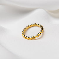 A gold-colored ring with a textured surface, placed on a white fabric background.