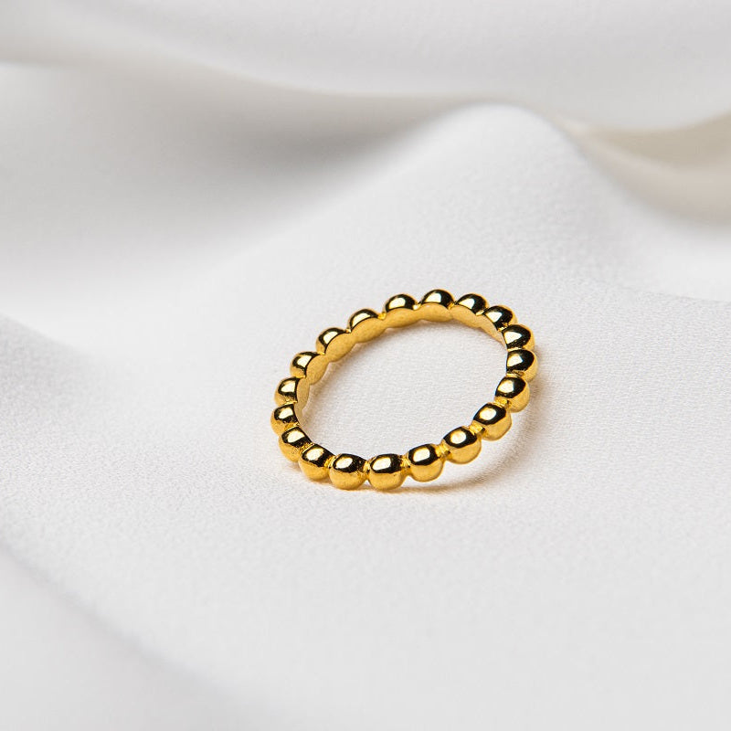 A gold-colored ring with a textured surface, placed on a white fabric background.