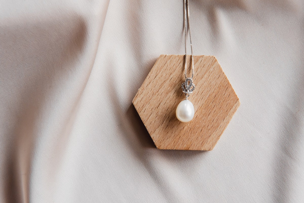 A sterling silver necklace with a white freshwater pearl and a small diamond cubic zirconia, displayed on a beige fabric surface.