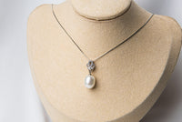 A sterling silver necklace with a white freshwater pearl and a small diamond cubic zirconia, displayed on a necklace stand.