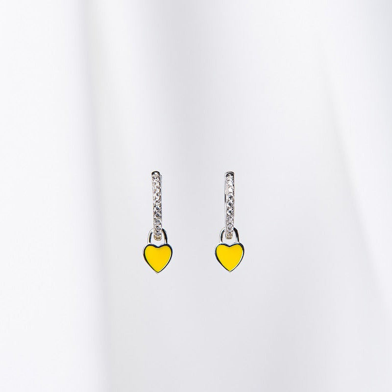 A pair of huggies earrings with yellow heart-shaped dangles on a silky white background.