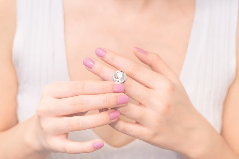 A womans hand wearing a large round silver ring featuring a dimple