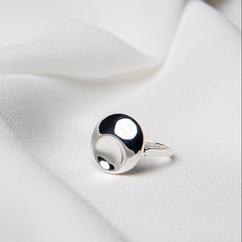 A polished silver ring with a solid pattern, displayed on a white fabric surface.
