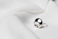 A polished silver ring with a solid pattern, displayed on a white fabric surface.