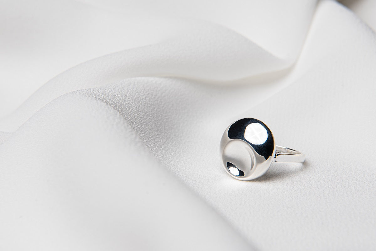 A polished silver ring with a solid pattern, displayed on a white fabric surface.