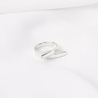 A polished, silver-colored band ring positioned on a white surface.