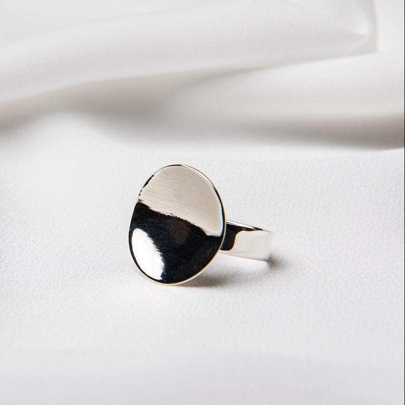 A polished silver disc shaped ring on a white cloth background