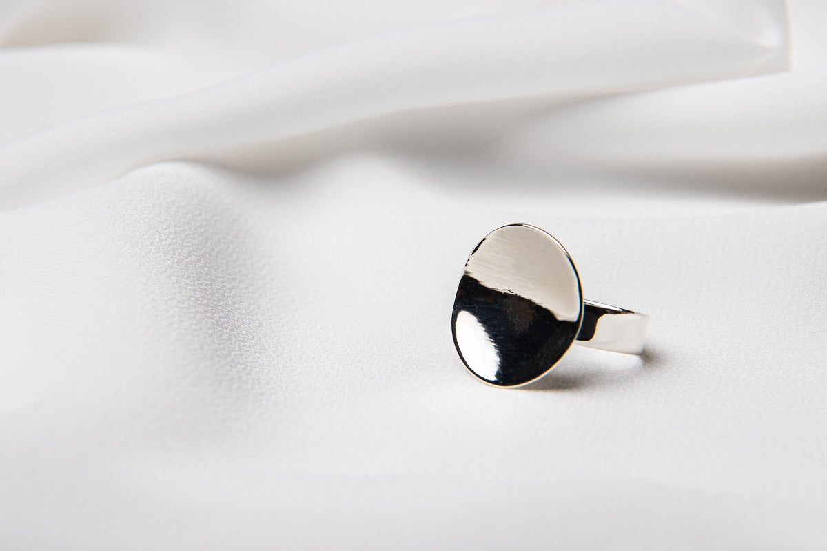 A polished silver disc shaped ring on a white cloth background