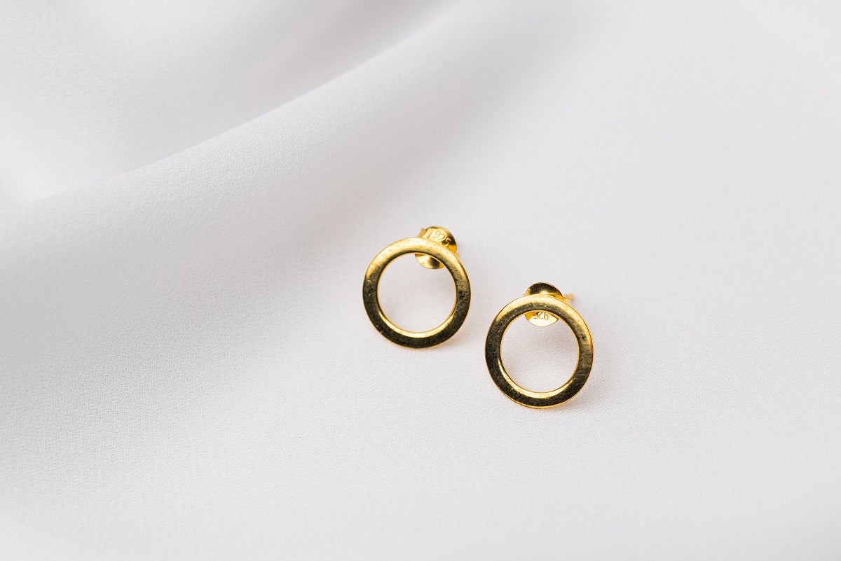 A pair of gold stud earrings with a butterfly back design, displayed against a white fabric background.