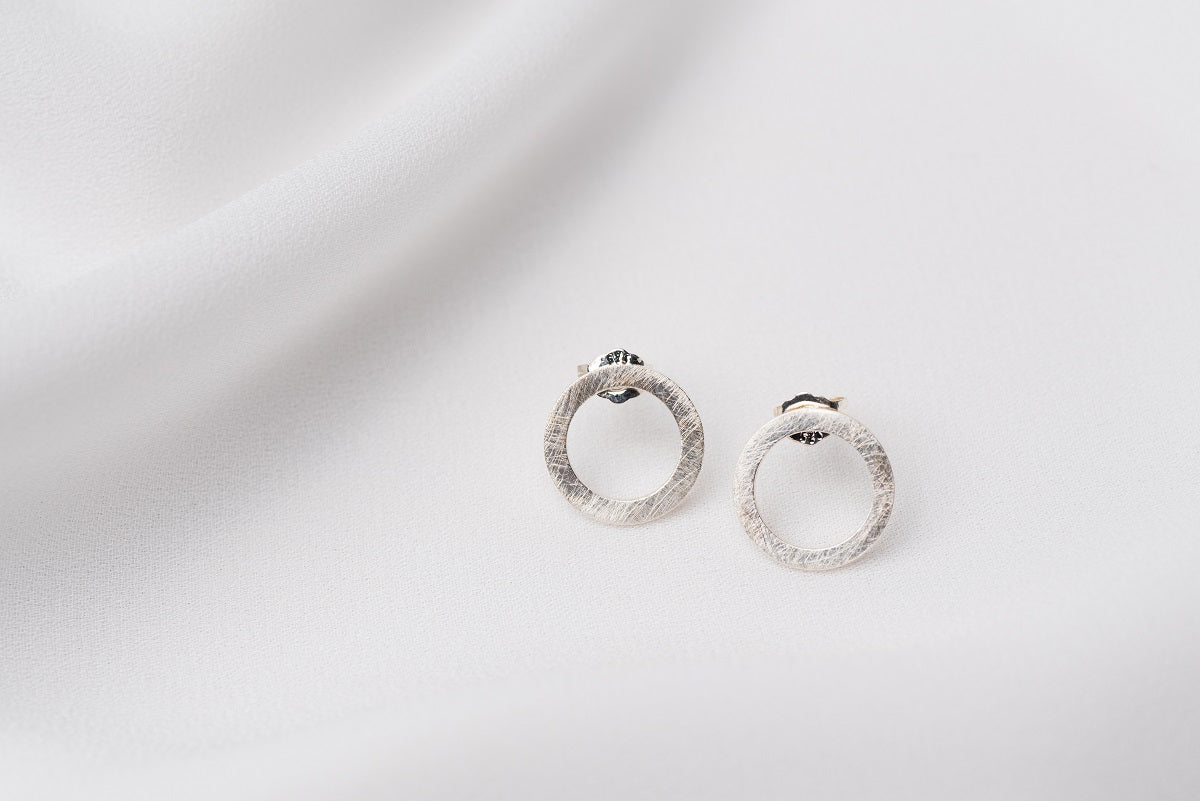 A pair of matte silver stud earrings with a butterfly back design, displayed against a white fabric background.