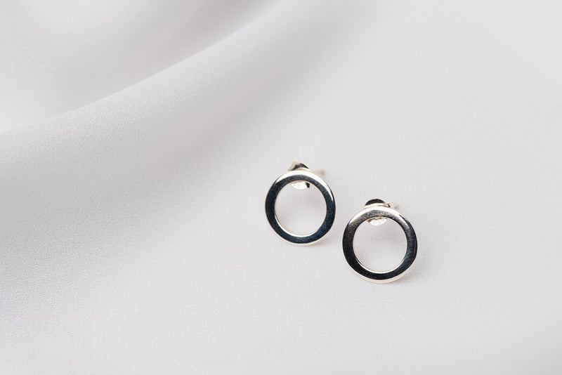 A pair of silver stud earrings with a butterfly back design, displayed against a white fabric background.