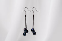 A pair of black drop earrings with 3 black pearls on a white background