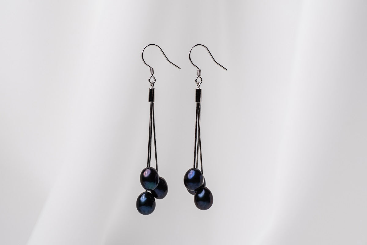 A pair of black drop earrings with 3 black pearls on a white background