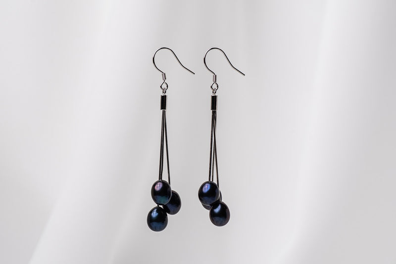A pair of black drop earrings with 3 black pearls on a white background