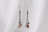 A pair of black drop earrings with 3 pearls on a white background