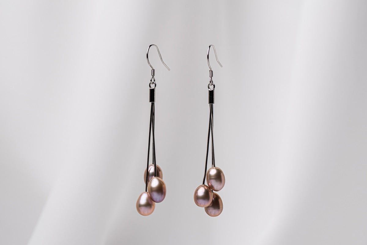 A pair of black drop earrings with 3 pearls on a white background