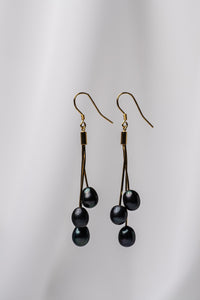 A pair of gold drop earrings with 3 lavender pearls on a white background