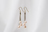 a pair of gold drop earrings with 3 champaigne pearls on a white background
