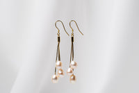 a pair of gold drop earrings with 3 champaigne pearls on a white background